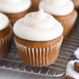 Several pumpkin cupcakes topped with whipped cream cheese frosting on wire cooling rack.