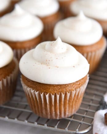Several pumpkin cupcakes topped with whipped cream cheese frosting on wire cooling rack.