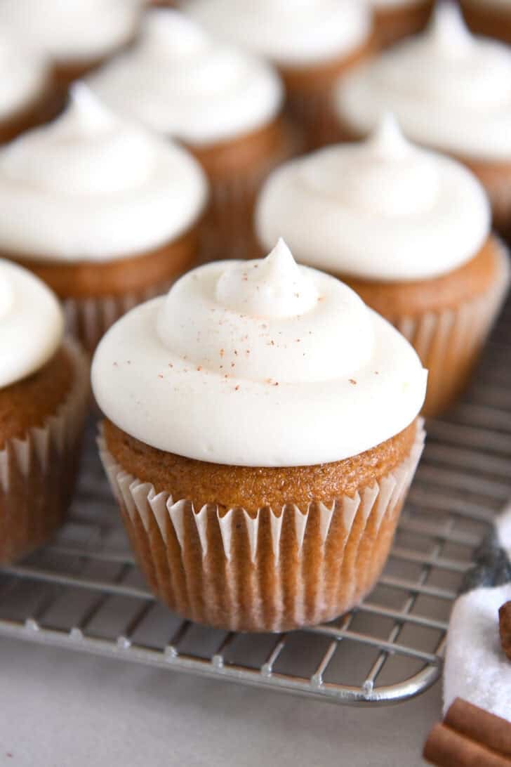 Several pumpkin cupcakes topped with whipped cream cheese frosting on wire cooling rack.