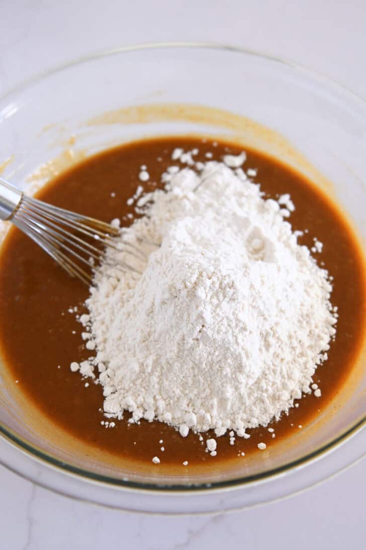 Glass bowl with pumpkin cupcake batter and flour with wire whisk.