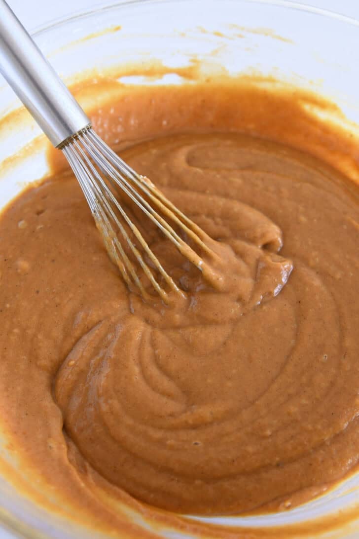 Pumpkin cupcake batter in glass bowl with wire whisk.