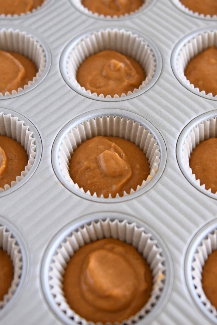 Metal cupcake tin with liners filled with pumpkin cupcake batter.