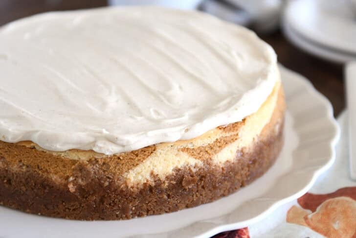 Baked pumpkin swirl cheesecake with white chocolate mousse layer on top on white serving platter.