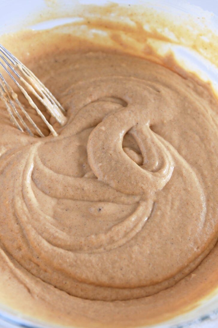 Pumpkin waffle batter in glass bowl with whisk.