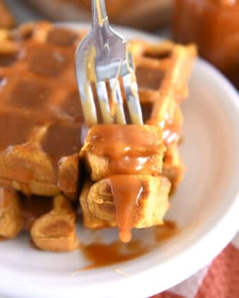 Fork lifting up two bites of pumpkin waffle with buttermilk caramel syrup dripping off.