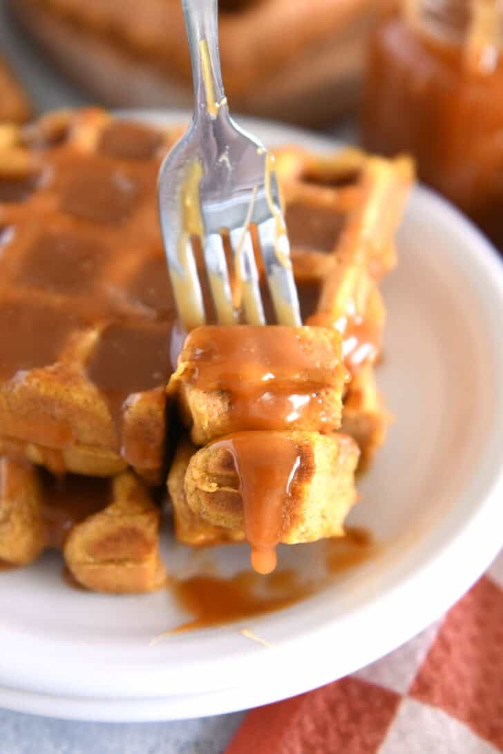 Fork lifting up two bites of pumpkin waffle with buttermilk caramel syrup dripping off.