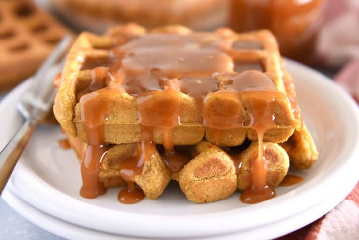 Two squares of pumpkin waffles on white plate smothered in buttermilk caramel syrup.