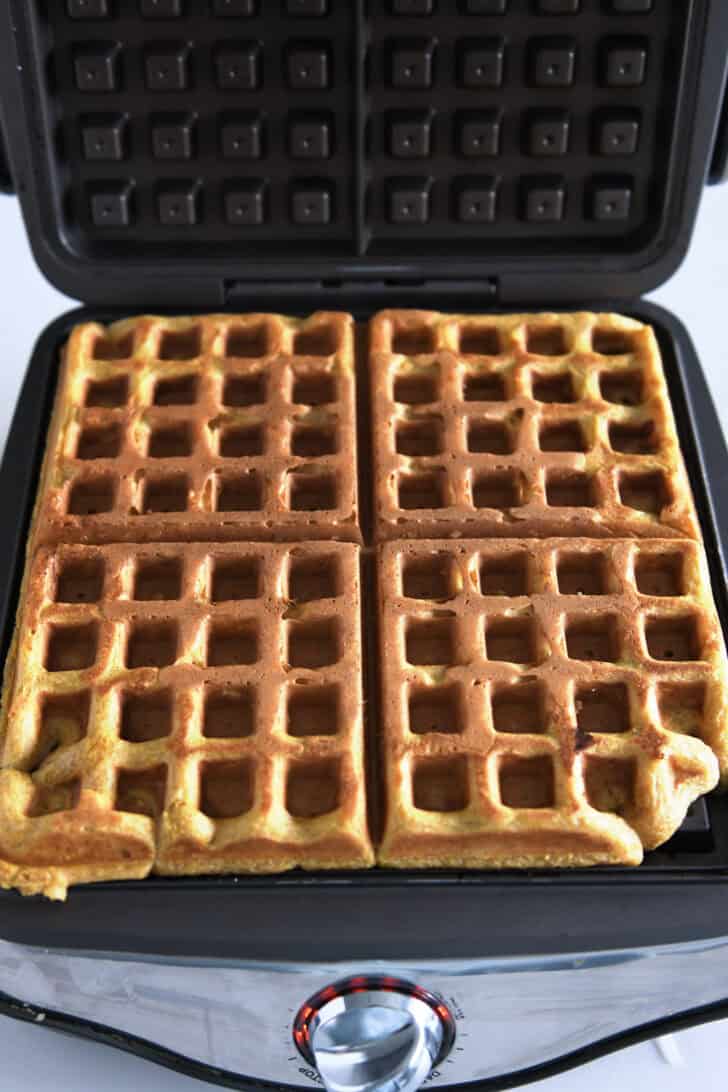 Pumpkin waffle baked in waffle maker. Lid open.