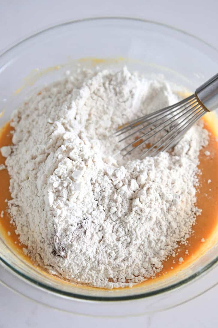 Glass bowl with dry ingredients in bowl with wet ingredients for pumpkin waffles.