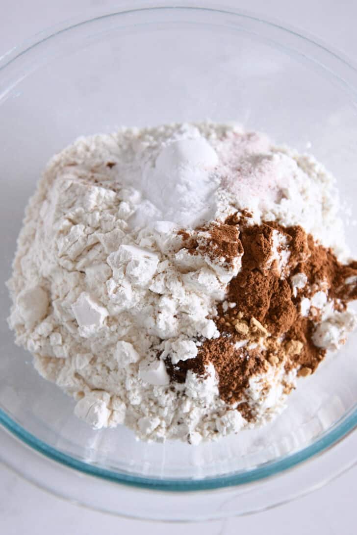 Glass bowl with flour, cinnamon, nutmeg, baking powder, baking soda and salt.