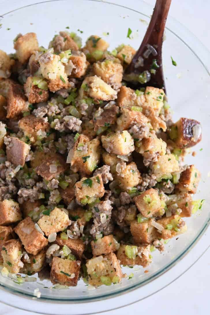 Glass bowl with toasted bread cubes, cooked sausage, cooked veggies and saturated with broth and eggs.