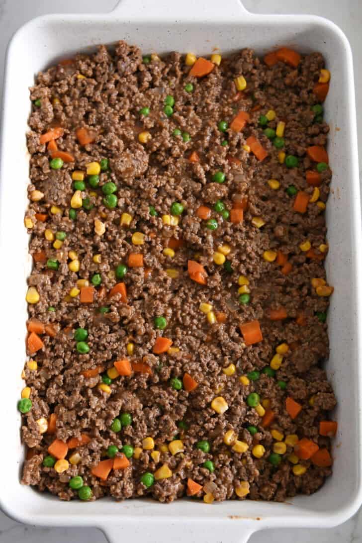 Top down view of a white casserole dish full of a meat and vegetable mixture.