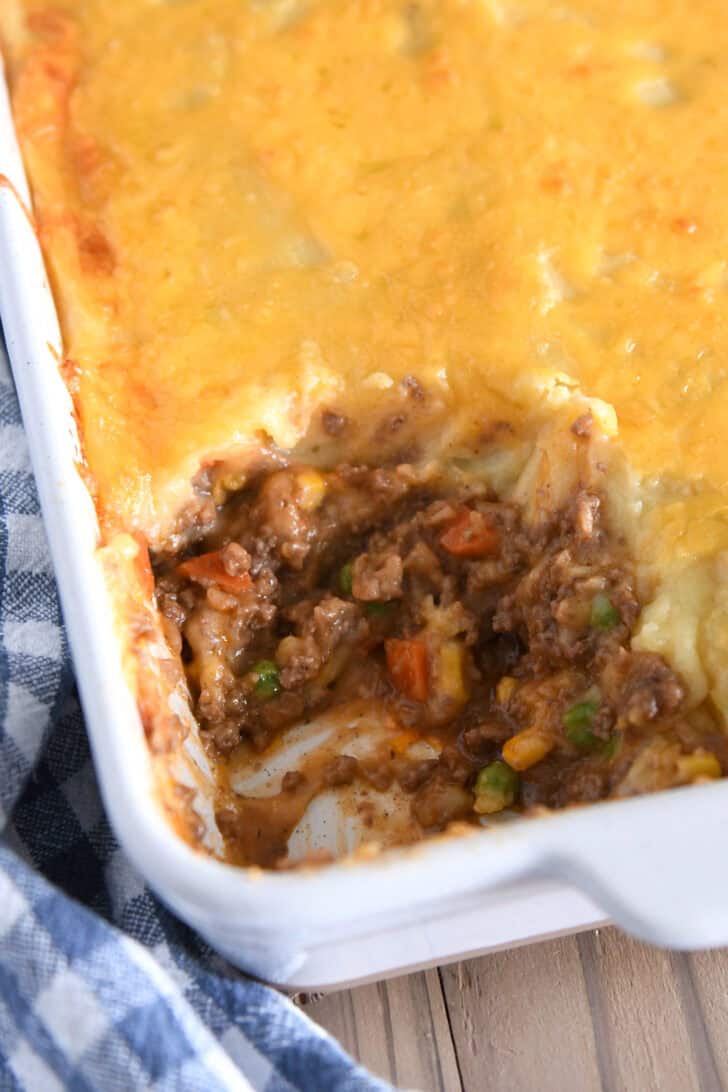 Top down view of a white casserole dish of shepherd's pie with a helping taken out.