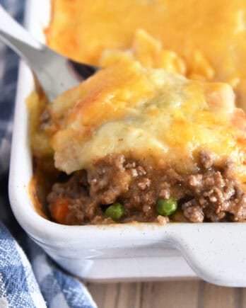 A spatula taking a helping of shepherd's pie out of a white casserole dish.