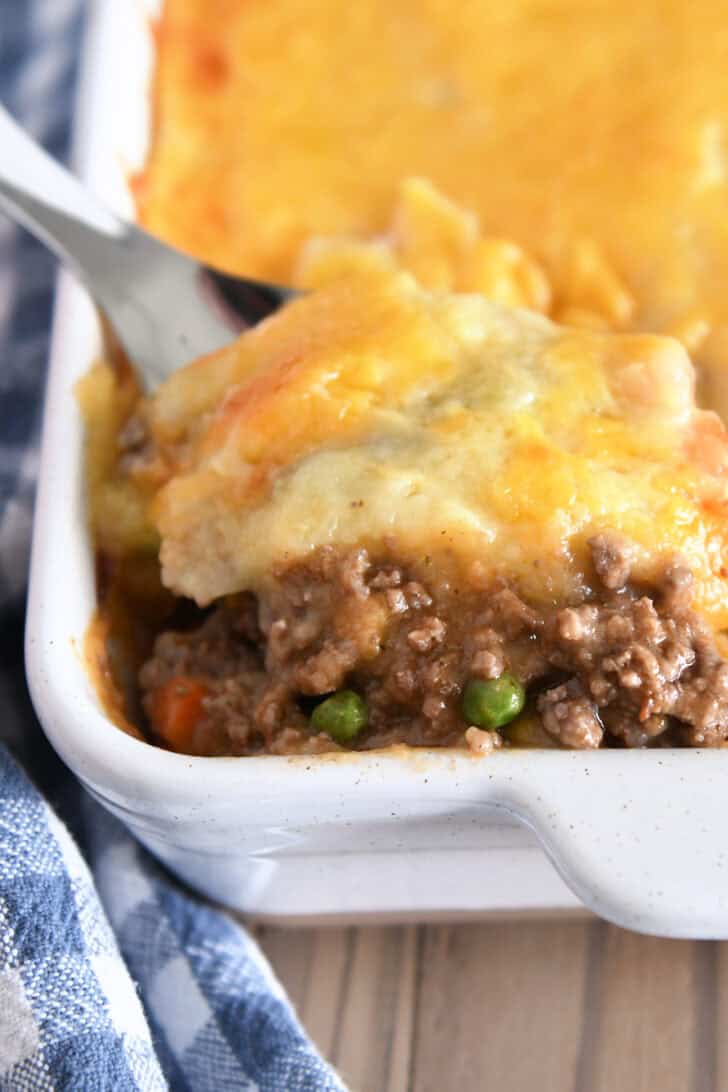 A spatula taking a helping of shepherd's pie out of a white casserole dish.