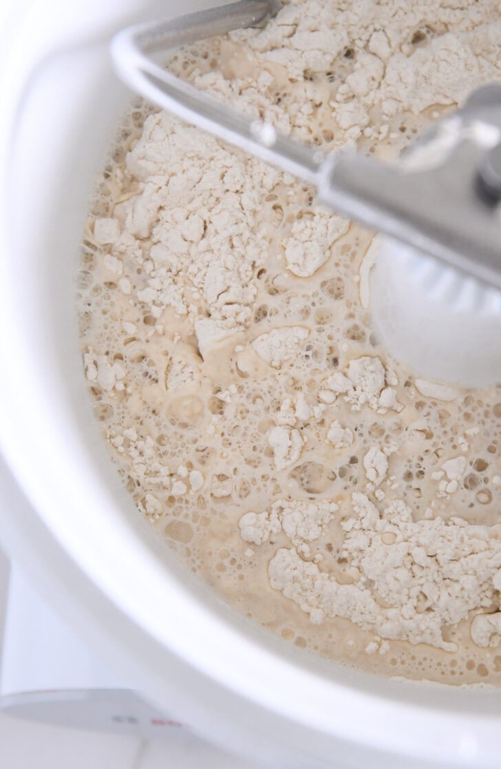 Water, flour and yeast in white Bosch universal mixer bowl with dough hook.