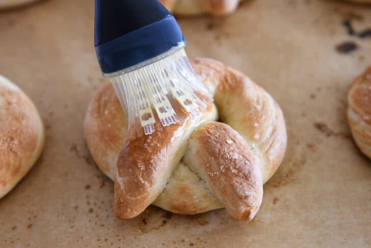 Using pastry brush to brush melted butter on hot, baked soft pretzel.