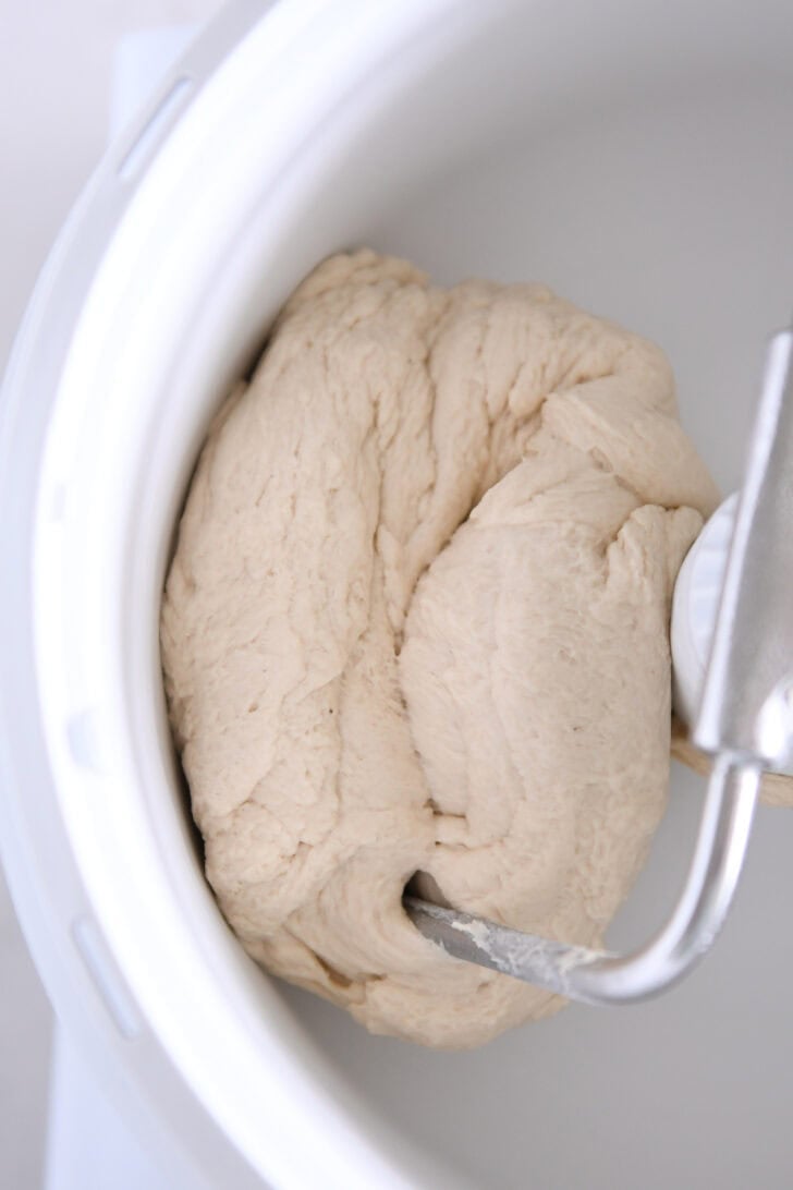 Soft ball of pretzel dough in white Bosch universal mixer bowl with dough hook.