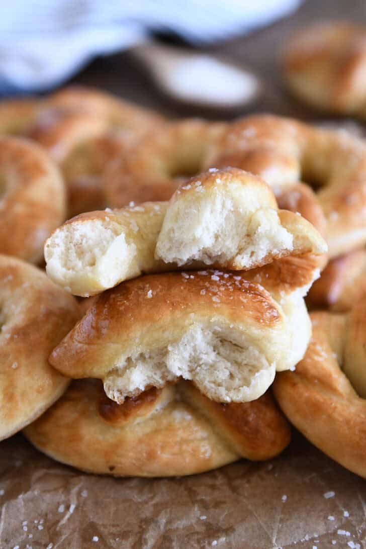 Two halves of soft pretzel torn apart and stacked on top of several homemade soft pretzels.