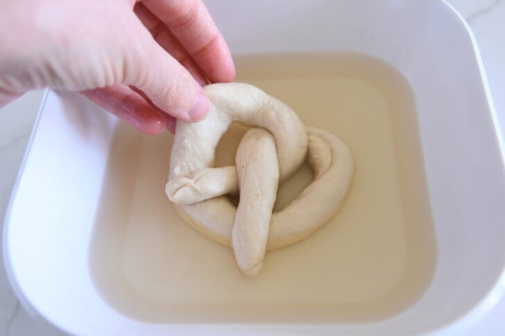 Dipping unbaked formed pretzel dough into water bath.