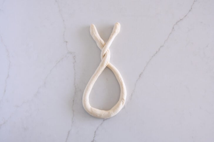 Forming long thin rope of pretzel dough into a pretzel by twisting ends.