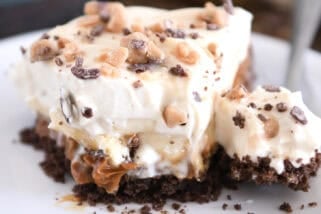 Slice of pie with chocolate cookie crust, dulce de leche, bananas, whipped cream and toffee on white plate.