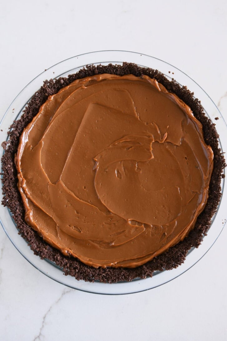 Dulce de leche spread across chocolate cookie crust in glass 9-inch pie plate.