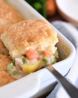 Spoon lifting out scoop of chicken pot pie filing for white 9X13-inch pan with baked biscuit on top.