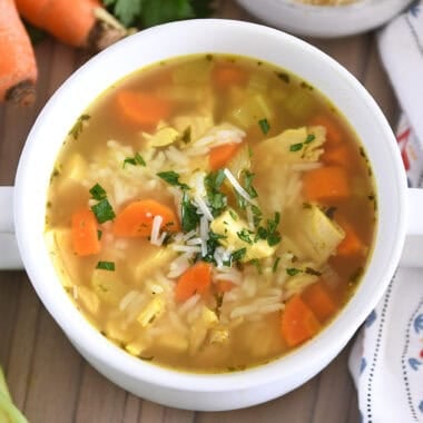 Top down view of chicken and rice soup in white bowl with handles topped with fresh parsley and Parmesan cheese.