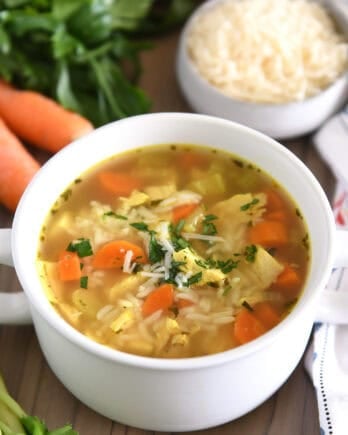 Chicken and rice soup in white bowl with handles topped with fresh parsley and Parmesan cheese.
