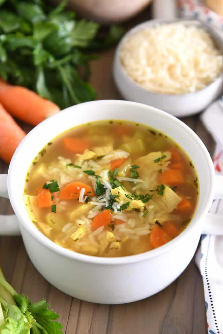 Chicken and rice soup in white bowl with handles topped with fresh parsley and Parmesan cheese.
