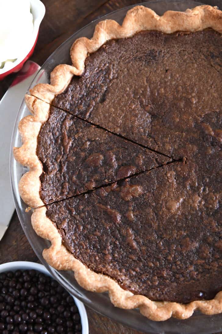 Top down view of chocolate chess pie with one piece cut but not removed from the pie.