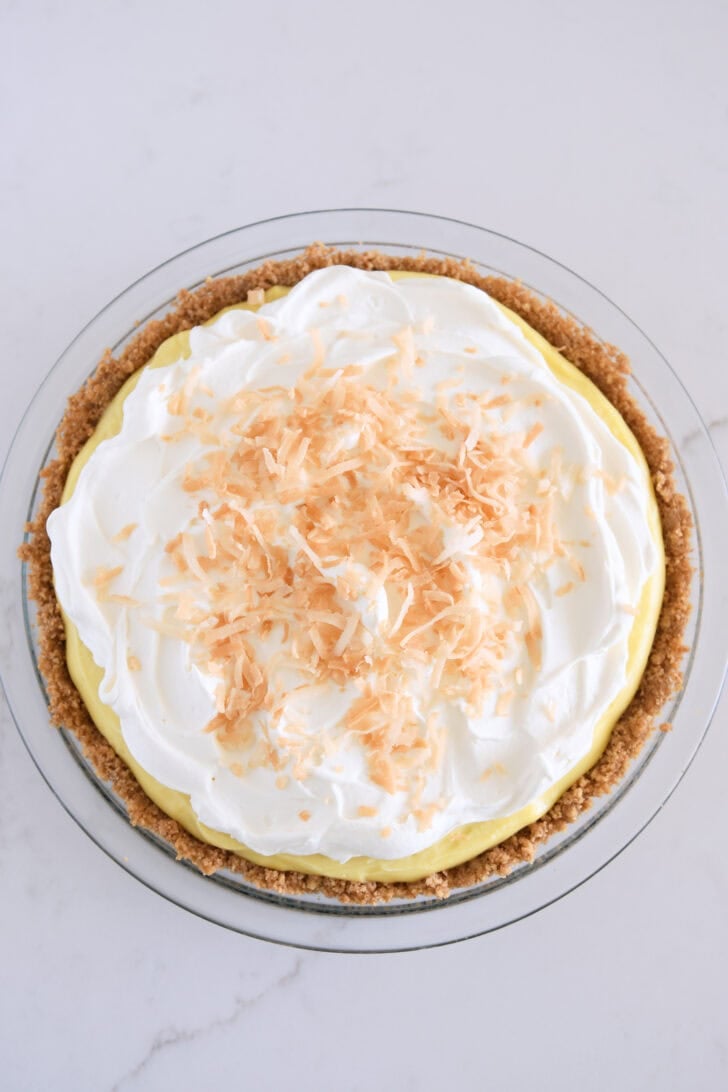 Glass 9-inch pie plate with graham cracker crust, filled with vanilla coconut cream pudding, topped with lightly sweetened whipped cream and toasted coconut.