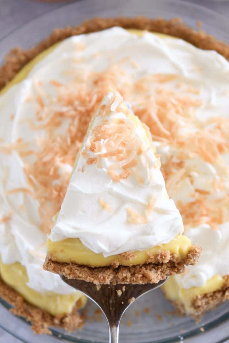 Top down view of pie server lifting triangle slice of coconut cream pie out of full pie.
