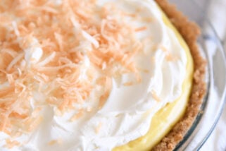Whole coconut cream pie in glass pie plate topped with whipped cream and toasted coconut.