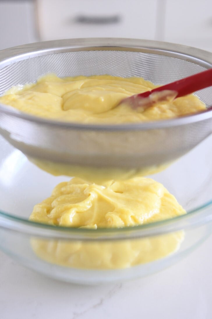 Straining coconut cream pie pudding through fine mesh strainer into glass bowl.