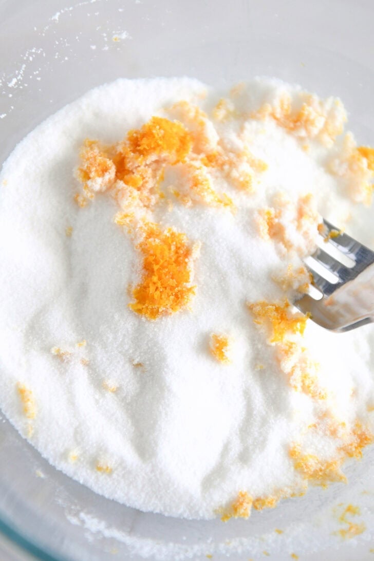 Glass bowl with granulated sugar and fresh orange zest.