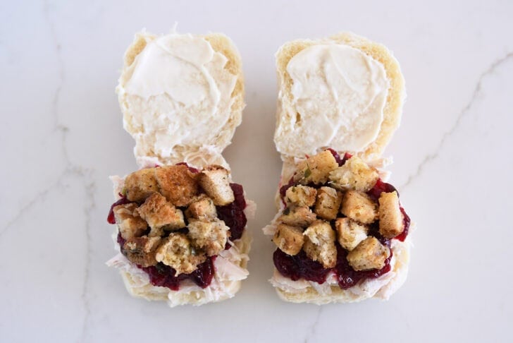 Two rolls open, spread with mayo, and layered with shredded turkey, cranberry sauce and stuffing.
