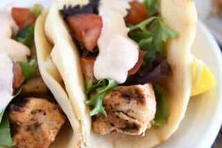 Flatbread grilled chicken wraps with lettuce, tomatoes, and creamy sauce on a white plate.