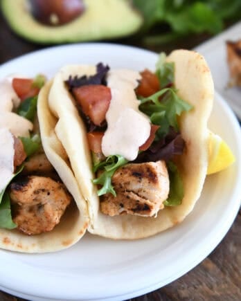 Flatbread grilled chicken wraps with lettuce, tomatoes, and creamy sauce on a white plate.