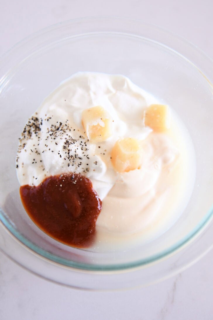 Top down view of a glass bowl with hot sauce, mayonnaise, yogurt, and spices.