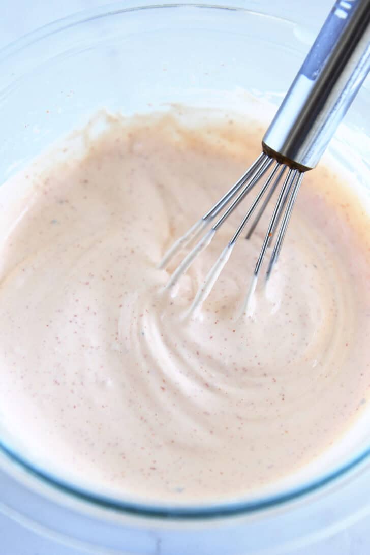 Top down view of a glass bowl with a creamy white sauce and a wire whisk.