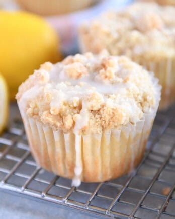 Lemon muffins with a crumb topping and white glaze on a cooling rack.