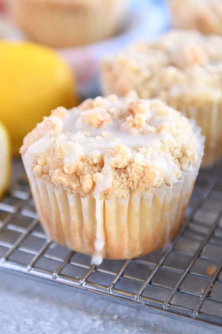 Lemon muffins with a crumb topping and white glaze on a cooling rack.
