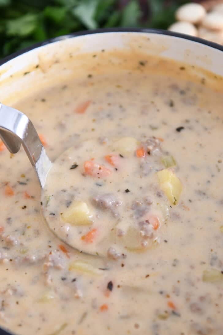 Ladle lifting up scoop of sausage potato soup in soup pot.
