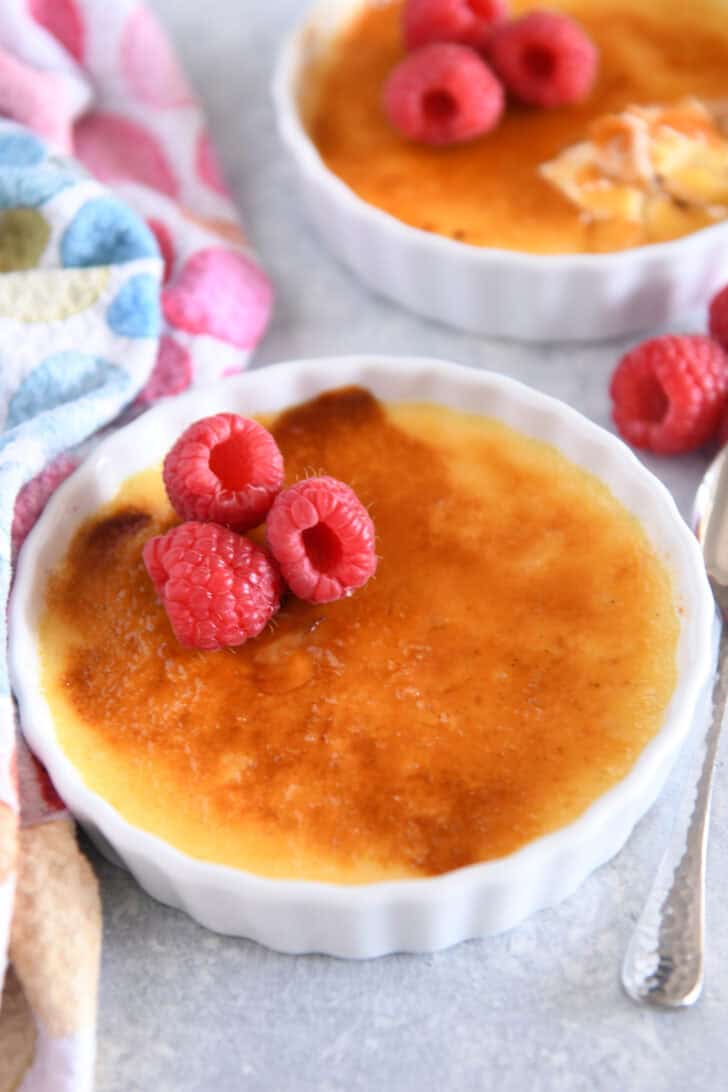 One creme brûlée in flat white ramekin with raspberries on the side.