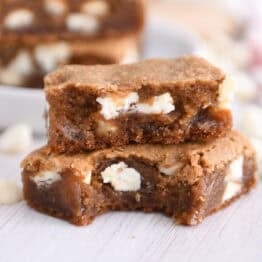 Two squares of white chocolate gingerbread blondie bars stacked with bite taken out of bottom bar.