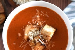 Top down view of white bowl filled with homemade tomato soup, homemade croutons and parmesan cheese.