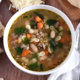 Top down photo of white bowl with broth, carrots, white beans, small pasta, and spinach.