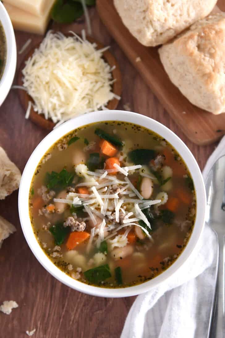 Top down photo of white bowl with broth, carrots, white beans, small pasta, spinach and Parmesan cheese.